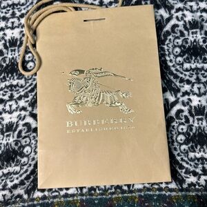 Burberry paper shopping bag with a gold logo and cloth handles.